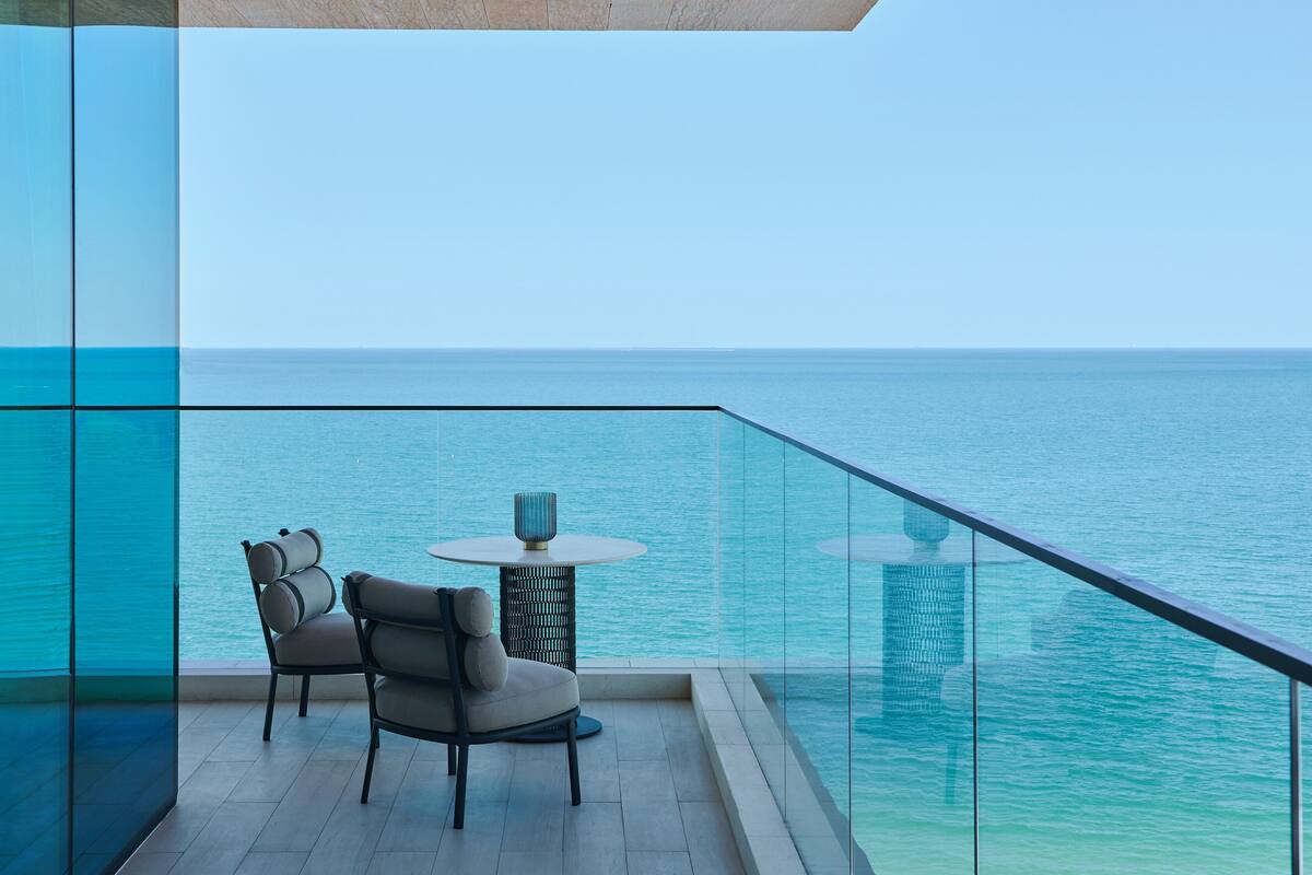 A balcony with a view of the sea, a round table, and two chairs.