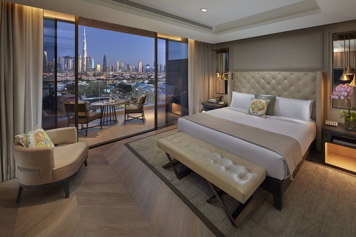A modern hotel room with a large bed, a seating area, and a view of a city skyline.