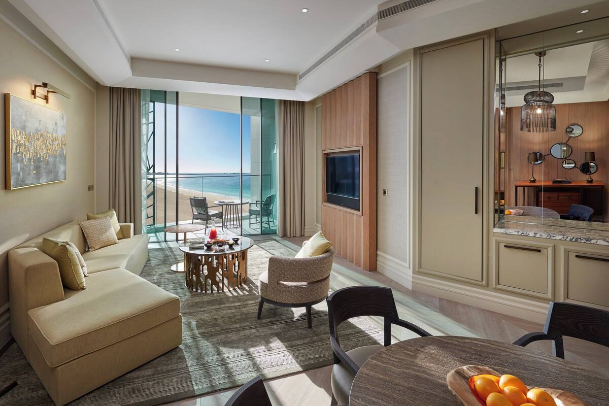 A modern living room with a sofa, chairs, a dining table, and a view of the beach.