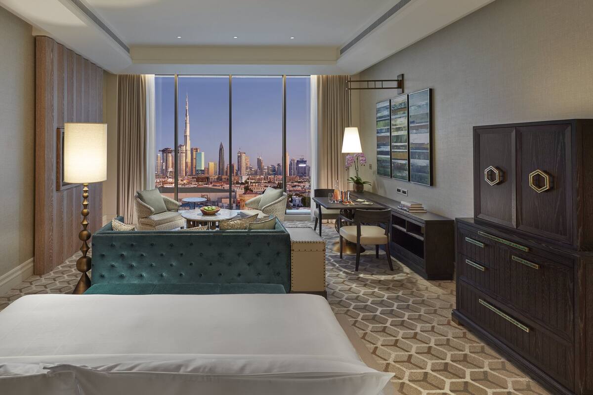 A hotel room with a large bed, a desk, a chair, and a view of a city skyline.