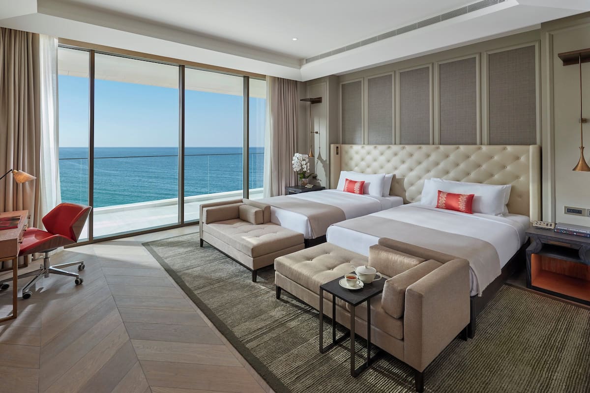A hotel room with two beds, a sofa, a desk, and a view of the ocean.