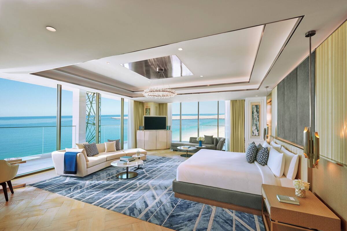 A modern hotel room with a large bed, a sofa, a TV, and a view of the sea.