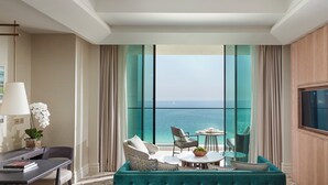 A hotel room with a large window offering a view of the sea, a sofa, a dining table, and a television mounted on the wall. - Mandarin Oriental Jumeira, Dubai (Dubai)