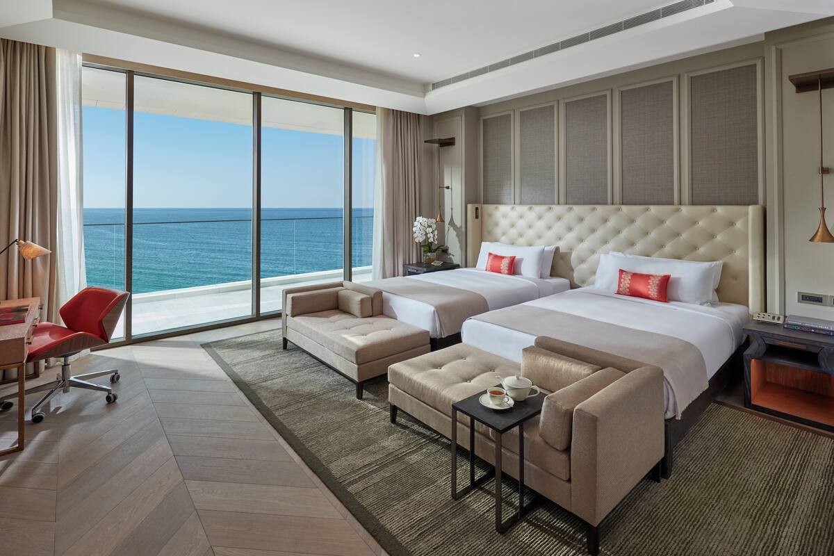 Habitación de hotel con dos camas, un escritorio, una silla y vistas al océano.