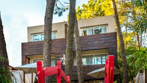 A wooden pathway leading to a modern building with a red gate, surrounded by lush greenery. - Mizu Hotel Boutique (Mar de Las Pampas)