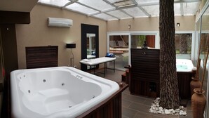 A spa room with a large bathtub, a massage table, and a view of the outdoor garden. - Mizu Hotel Boutique (Mar de Las Pampas)