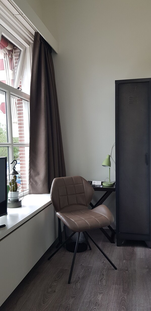 Una habitación con ventana, un escritorio con computadora, una silla, una lámpara y un armario.