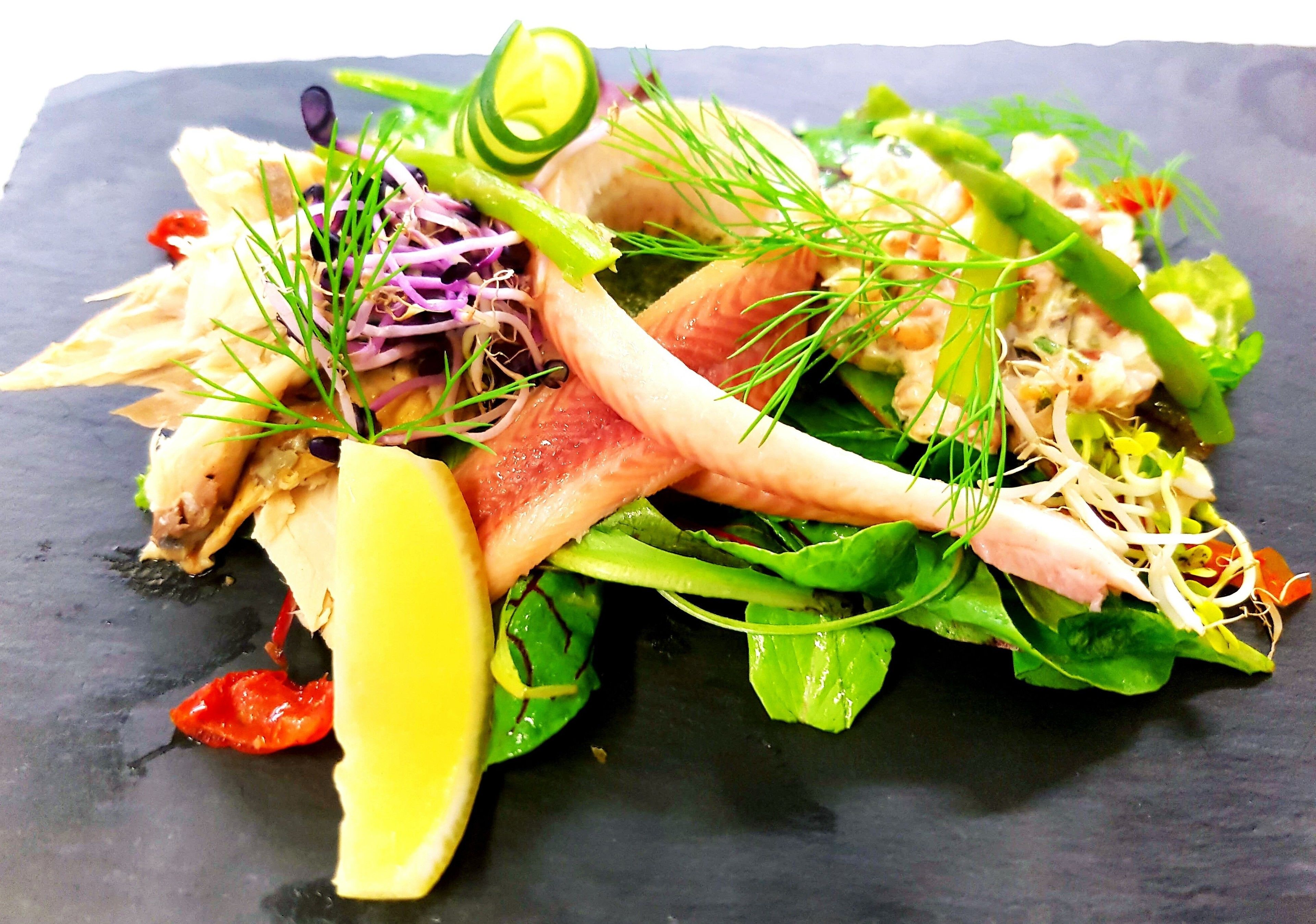 En sallad med olika grönsaker och sorters kött, serverad på en skiffertallrik.