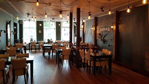 Een restaurantinterieur met houten tafels en stoelen, hangende lampen en een muurschildering.