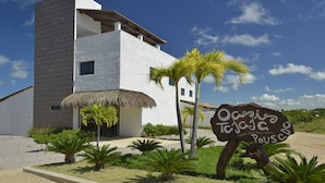 A modern building with a white facade and a thatched roof, surrounded by palm trees and a sign reading "Oasis Teja'a Pouscadero". - Oasis Tajaja (Conde)