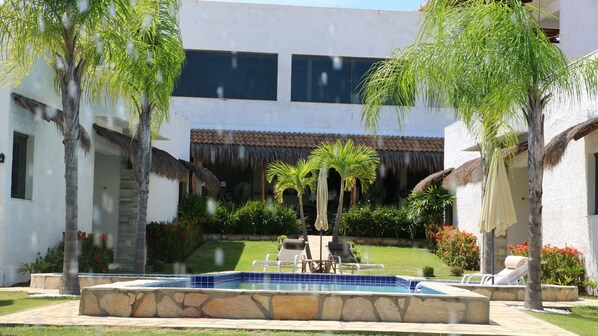 Un área de piscina con sillones de descanso, una piscina de piedra y una estructura con techo de paja.