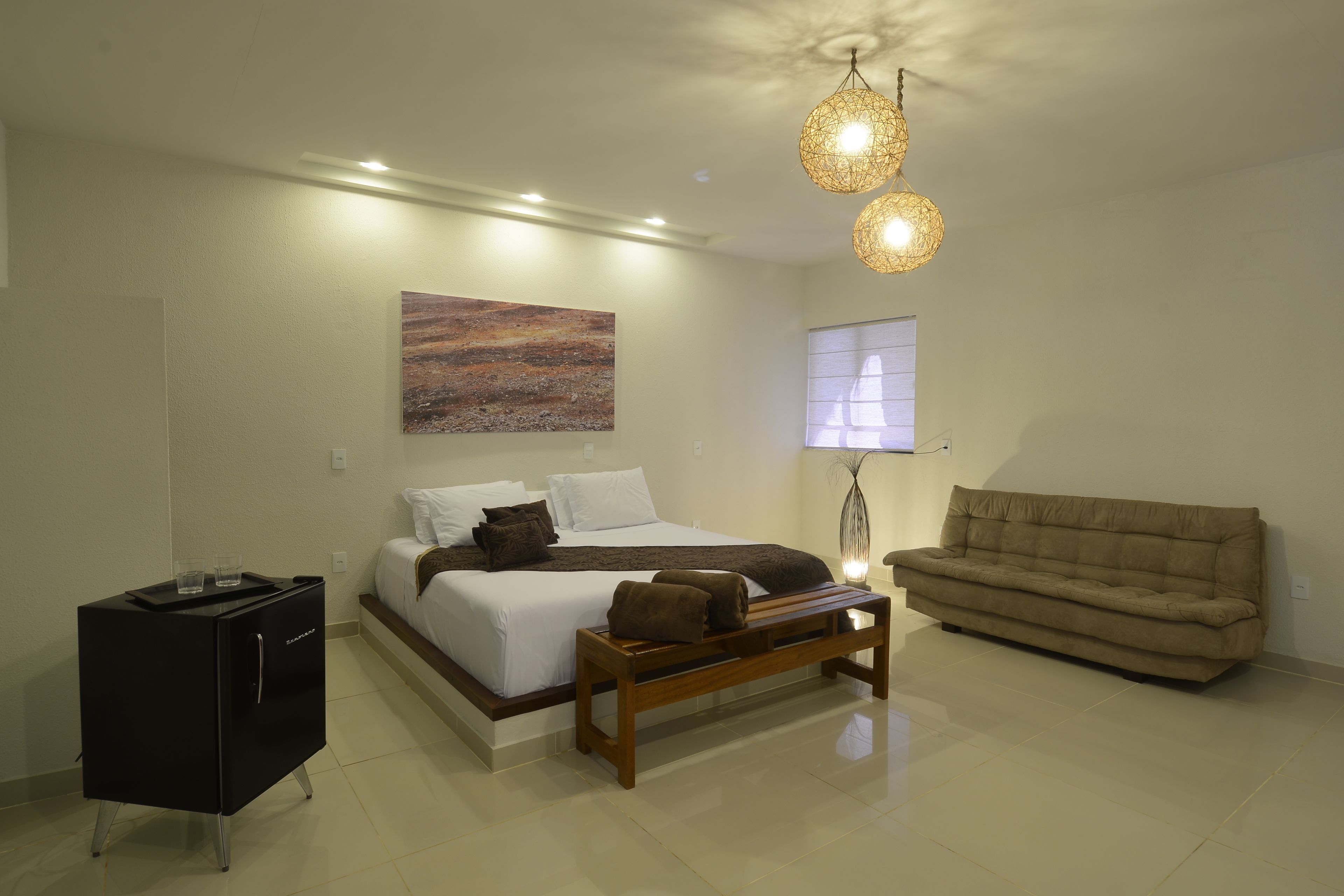 Quarto moderno com cama, mesa de cabeceira, banco e sofá.
