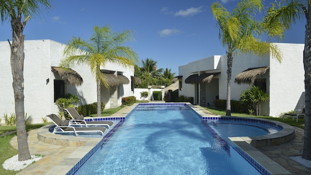 A swimming pool with lounge chairs and palm trees, surrounded by white buildings with thatched roofs. - Oasis Tajaja (Conde)