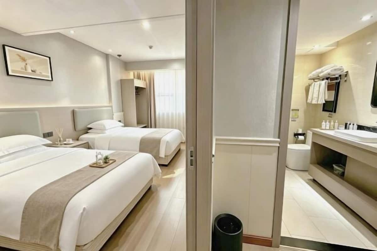 Ein Hotelzimmer mit zwei Betten, einem Badezimmer inklusive Waschtisch und einem großen Spiegel.