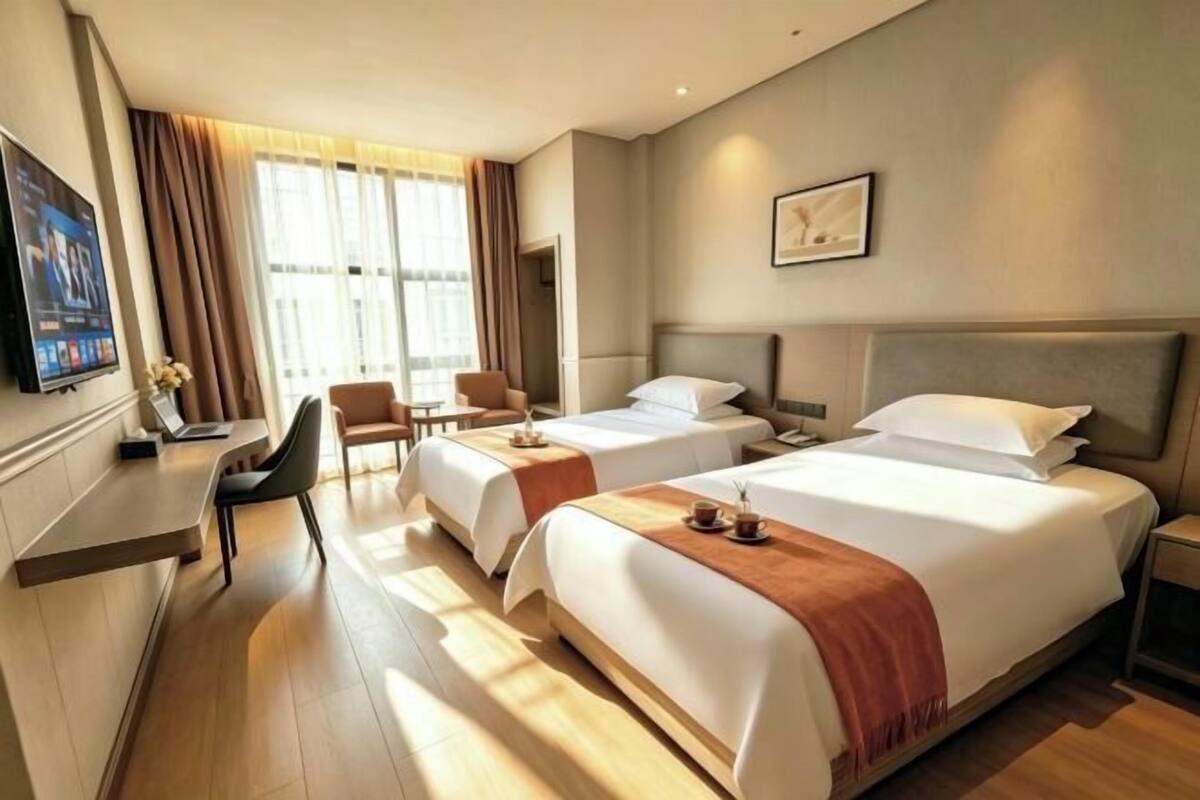 Ein Hotelzimmer mit zwei Betten, einem Schreibtisch, einem Sessel und einem Fernseher.