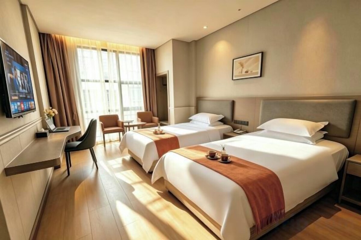 A hotel room with two beds, a desk, a chair, and a television.