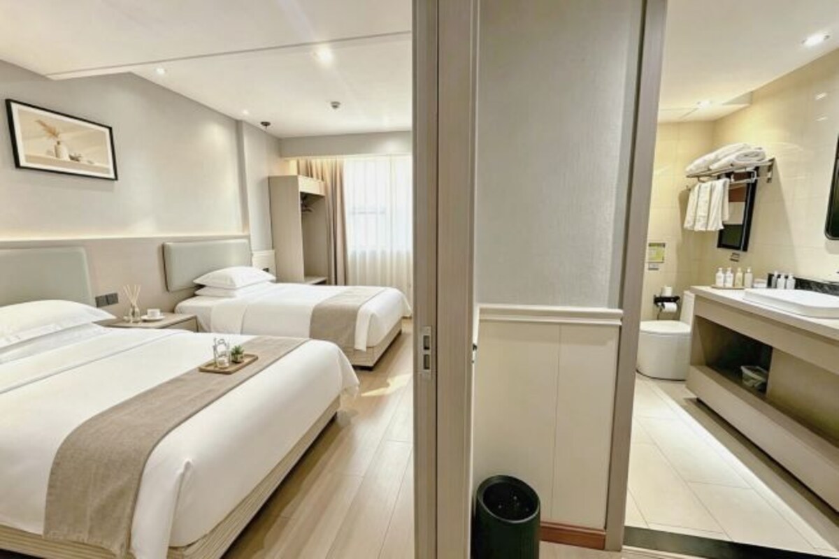 A hotel room with two beds, a bathroom with a vanity, and a large mirror.