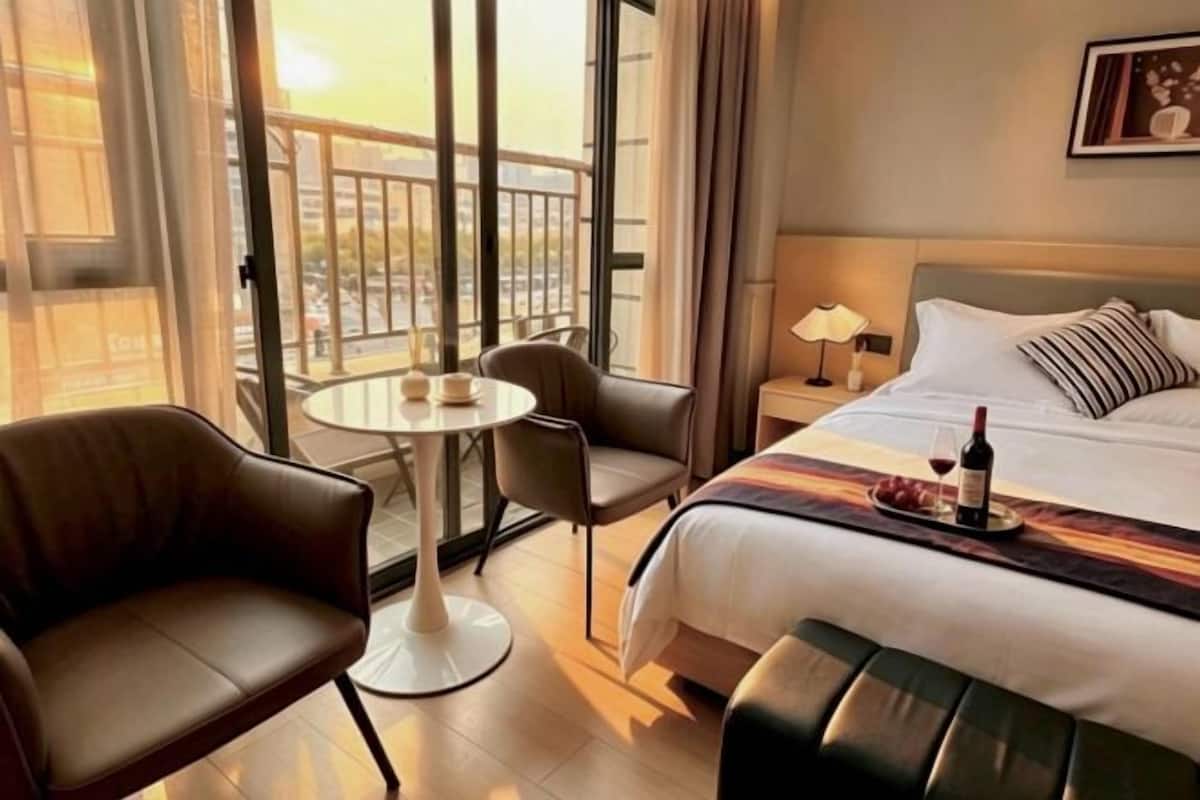 Ein Hotelzimmer mit einem Bett, einem kleinen runden Tisch, zwei Stühlen, einem Nachttisch und Blick ins Freie.