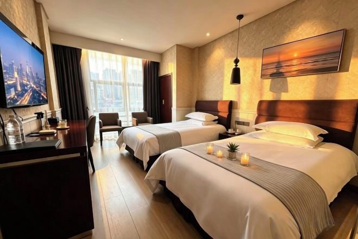 A hotel room with two beds, a desk, a TV, and a large window.