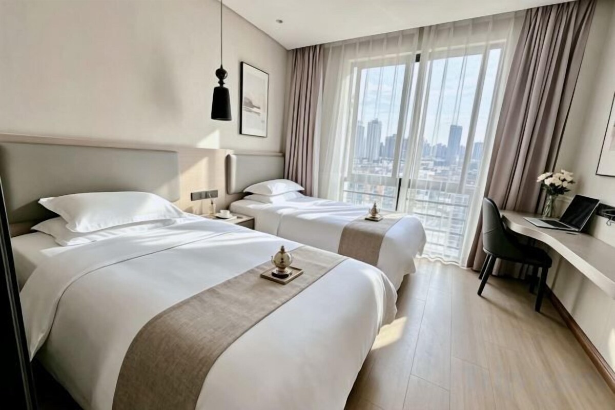 A hotel room with two beds, a desk, and a view of the city.