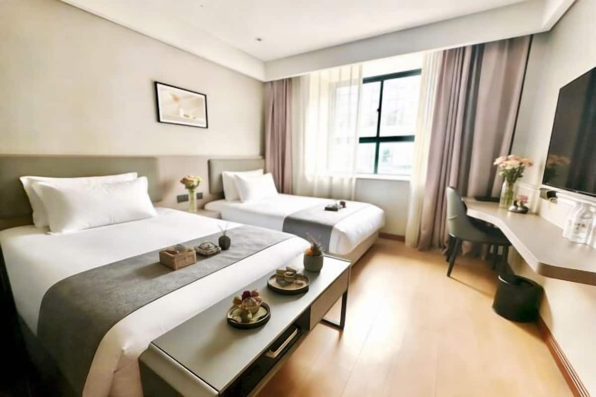 Ein Hotelzimmer mit zwei Betten, einem Schreibtisch, einem Stuhl, einem Fernseher und einem Fenster mit Vorhängen.