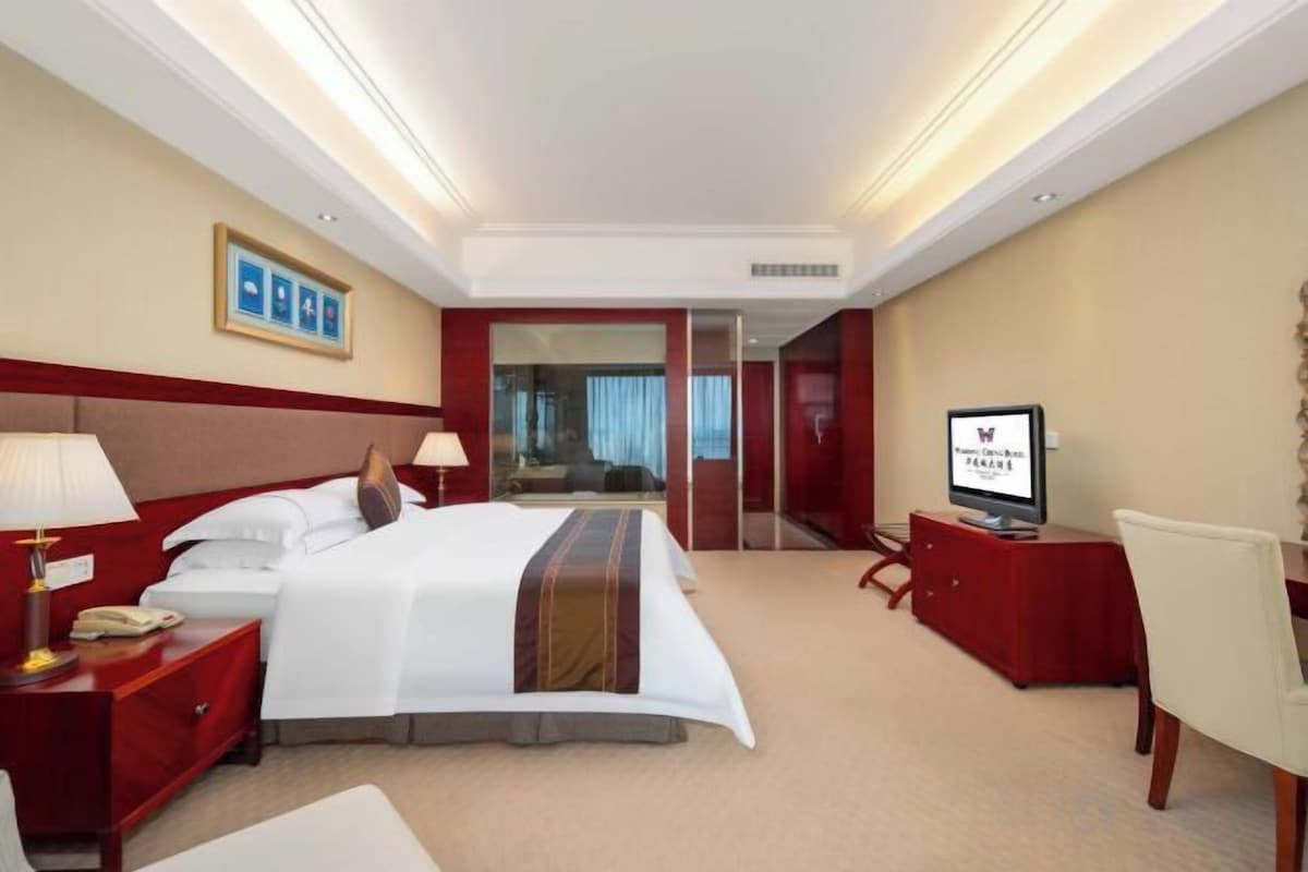 A hotel room with a bed, bedside tables, a TV, and a desk with a chair.