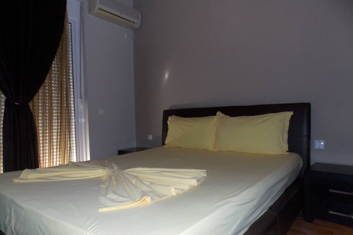 A neatly made bed with a folded towel, a bedside table, and a wall-mounted air conditioning unit.