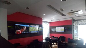 Ein Restaurant mit mehreren Fernsehbildschirmen, die Sportveranstaltungen zeigen, roten Wänden und schwarzen Stühlen.