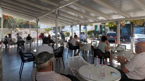 Ein Straßencafé mit Tischen, Stühlen und einem Vordach, mit Blick auf die Straße.