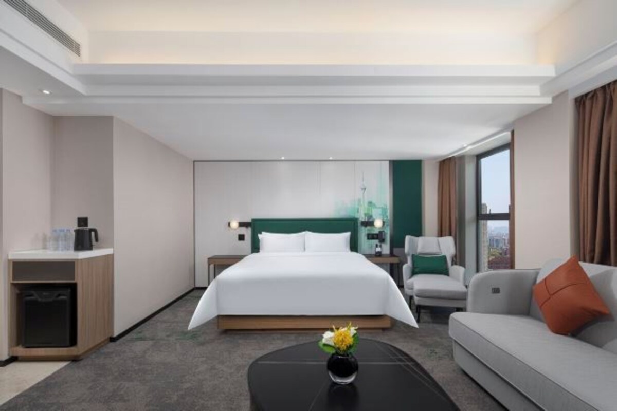 A hotel room with a large bed, a sofa, a coffee table, and a view of the city.