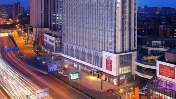 A high-rise hotel with a modern glass facade, located in an urban setting with visible traffic and other buildings in the background. - Hampton by Hilton Chengdu Waishuangnan (Chengdu)