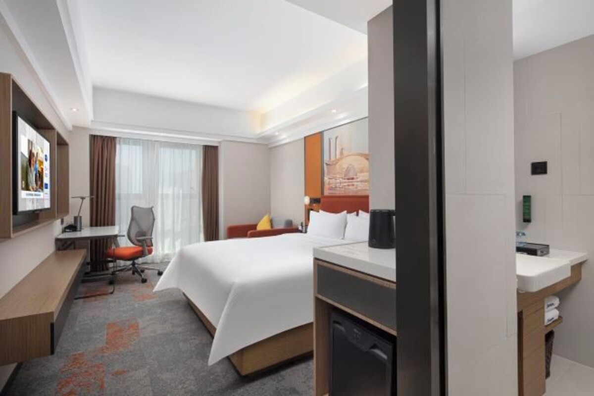 A hotel room with a bed, desk, chair, and a small kitchenette.