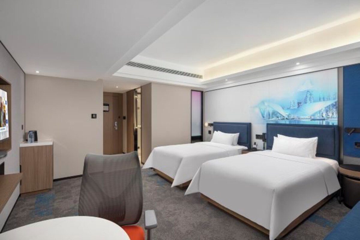 A hotel room with two beds, a desk, a chair, and a painting on the wall.