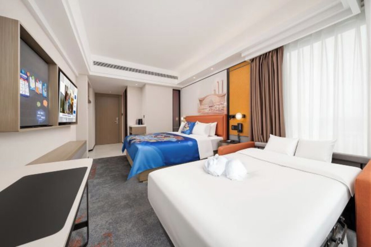 A hotel room with a large bed, a smaller bed, a desk, a TV, and a bathroom.