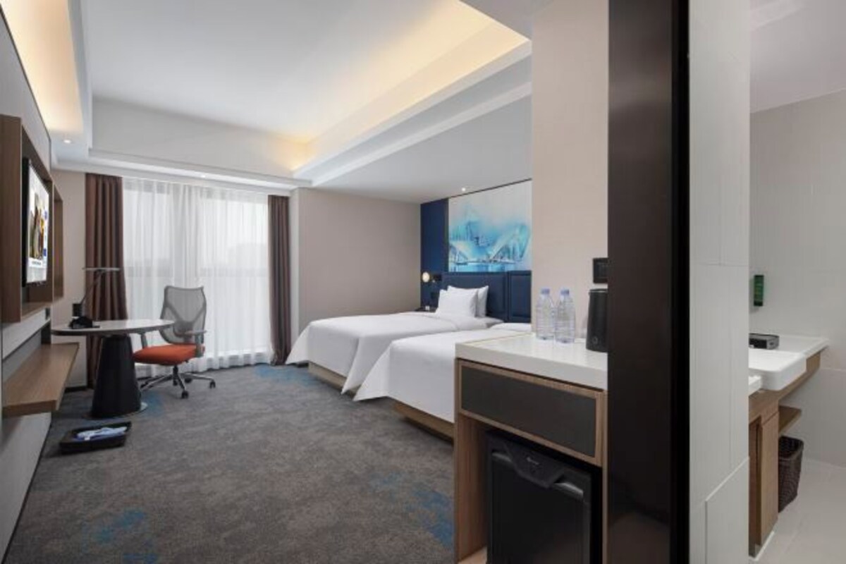 A hotel room with a bed, a desk, a chair, a small table, and a window with curtains.