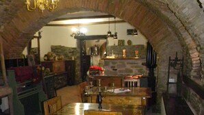 An arched stone room with a wooden dining table, chairs, and a chandelier. - Casa Bertha (Sighisoara)