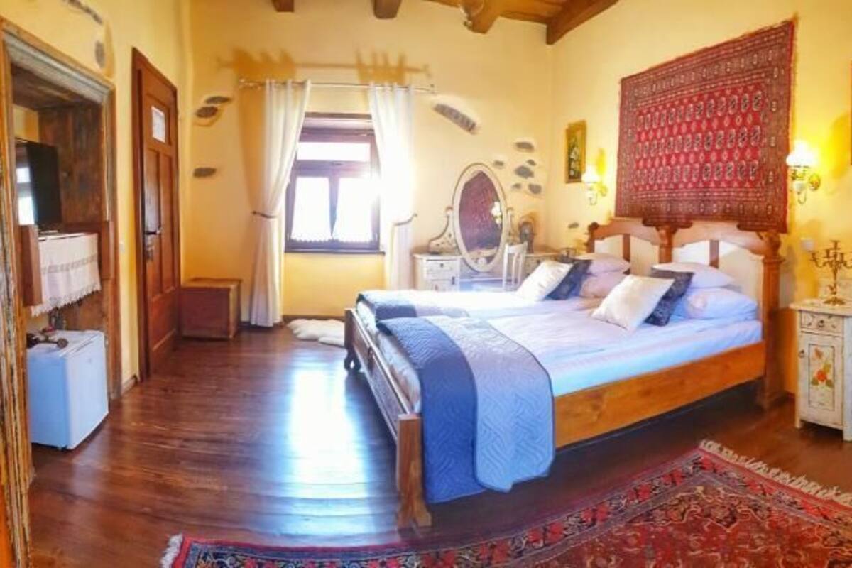 A bedroom with a wooden bed, a nightstand, a chair, and a table with a floral tablecloth.