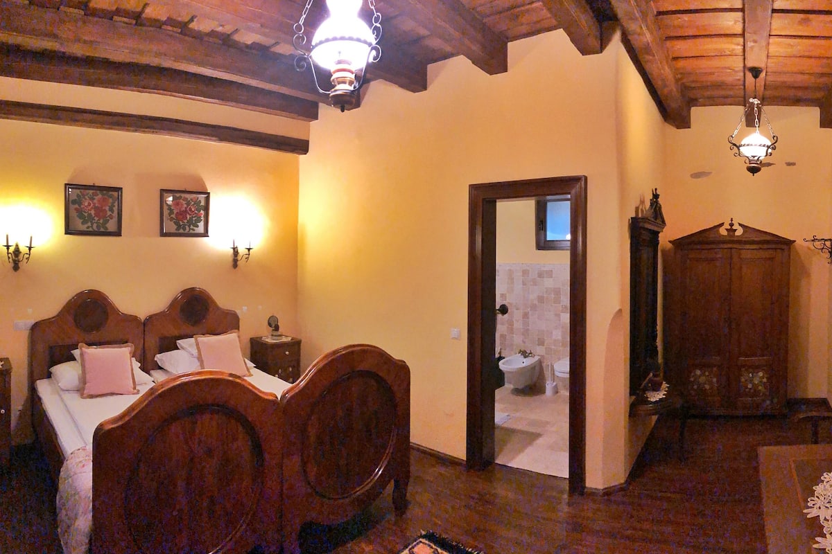 A bedroom with a wooden bed, a nightstand, a dresser, and a bathroom visible through an open door.