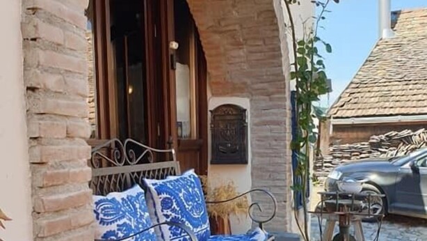 A stone archway leading to a bench with a blue patterned cushion, a metal lamp post, and a car parked nearby. - Casa Bertha (Sighisoara)