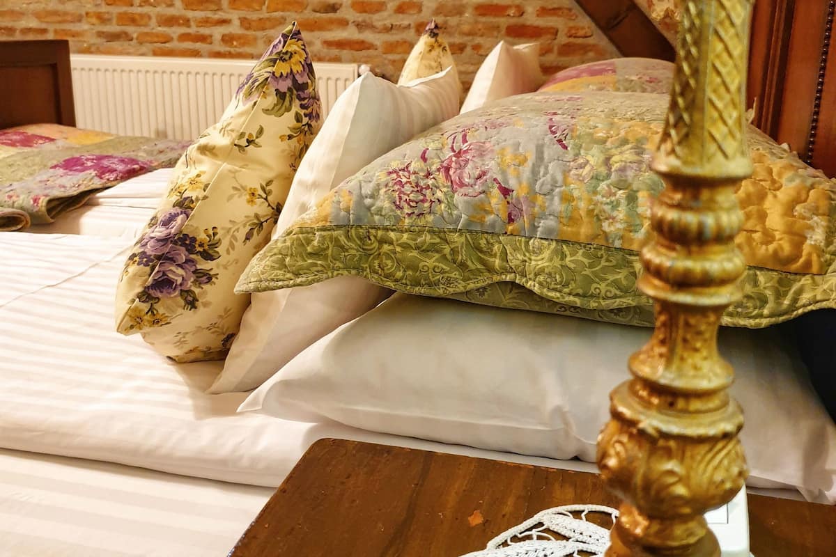 A bed with floral-patterned pillows and a wooden nightstand with a lace doily.