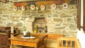 A rustic stone wall with a fireplace, wooden furniture, and a hanging plate rack. - Casa Bertha (Sighisoara)