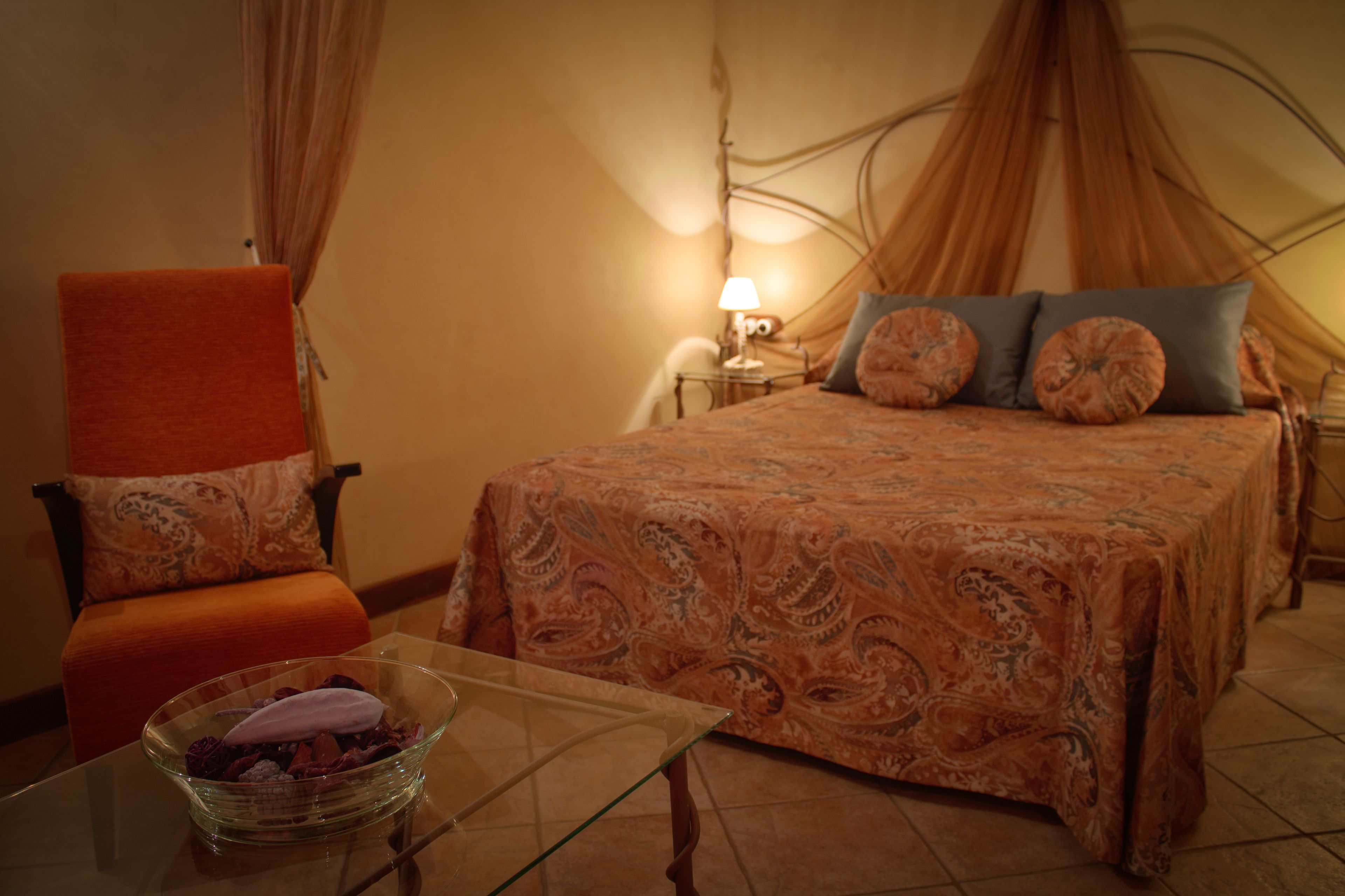 A bedroom with a bed, a chair, a nightstand, and a lamp.