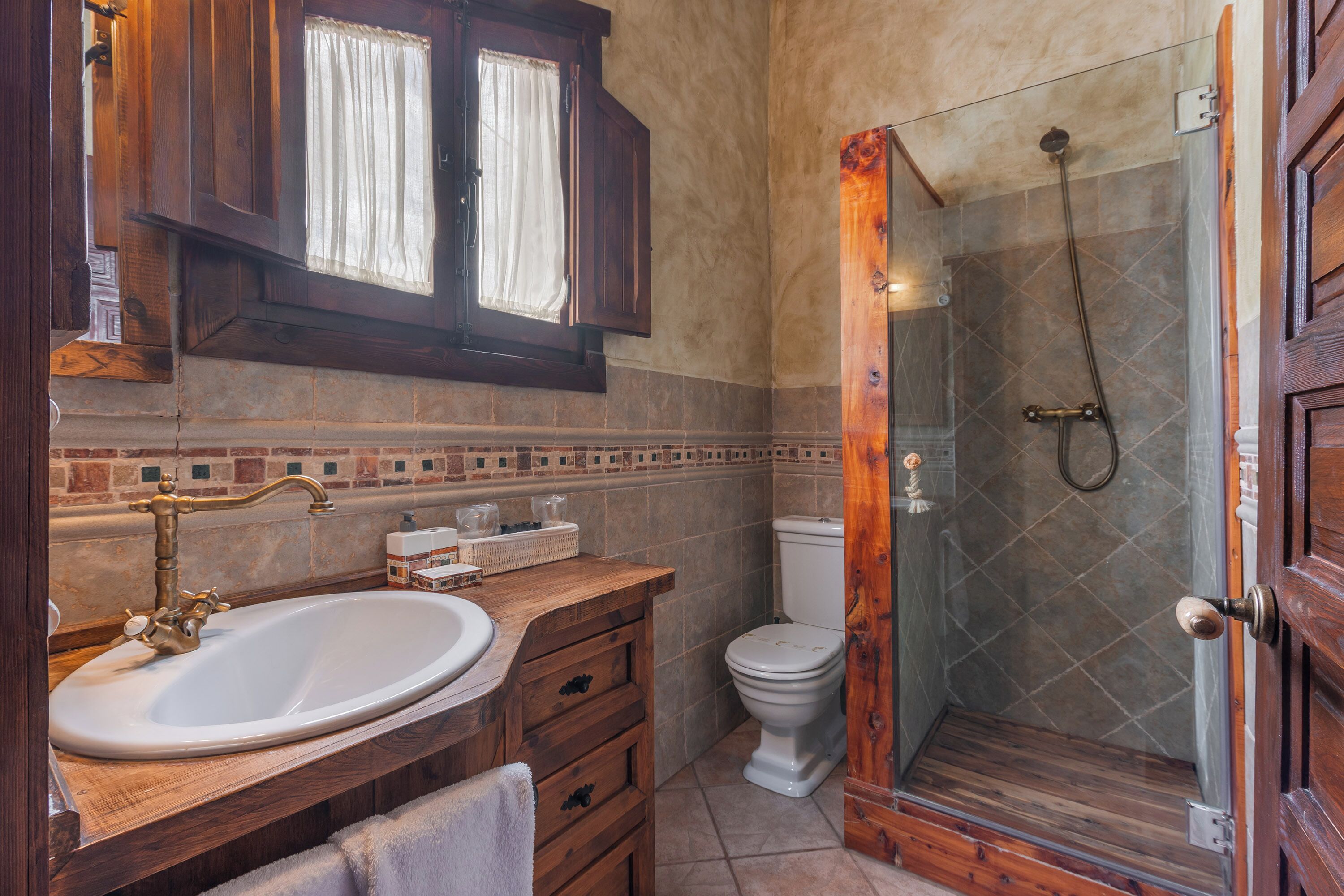 Een badkamer met een houten wastafelmeubel, een witte wastafel, een toilet en een douche met glazen wanden.