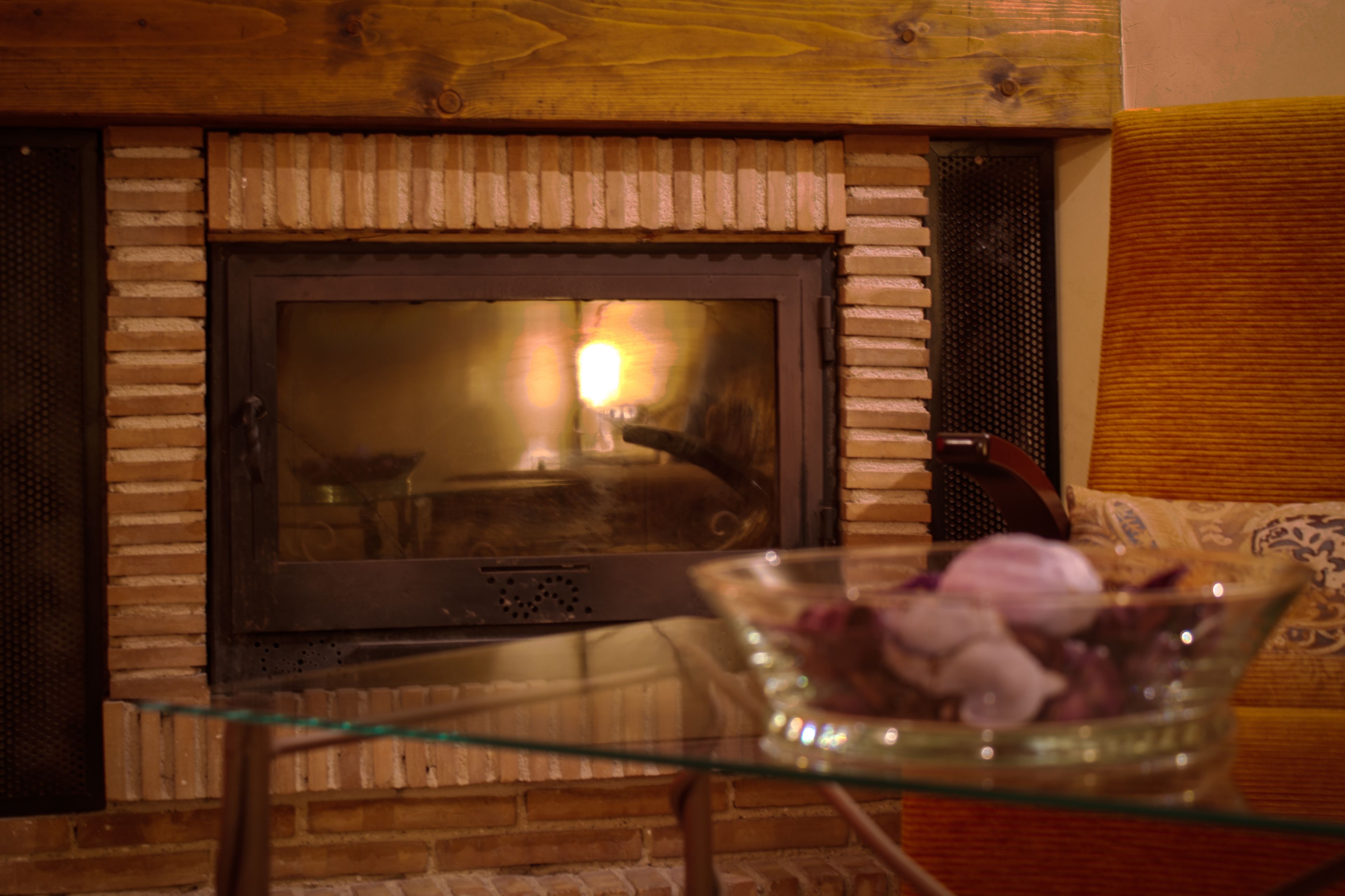 A fireplace with a glass table in front, a brick wall, and a wooden ceiling.