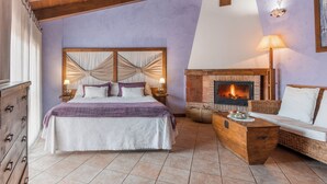 Un dormitorio con una cama grande, cabecera de madera, chimenea, sofá y mesita de noche con lámpara.