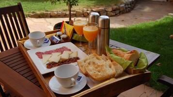 A breakfast tray with cheese, ham, bread, and juice on a wooden table outdoors.