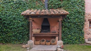 Chimenea de piedra al aire libre con techo de tejas, rodeada de escalones de piedra y cestas de leña.