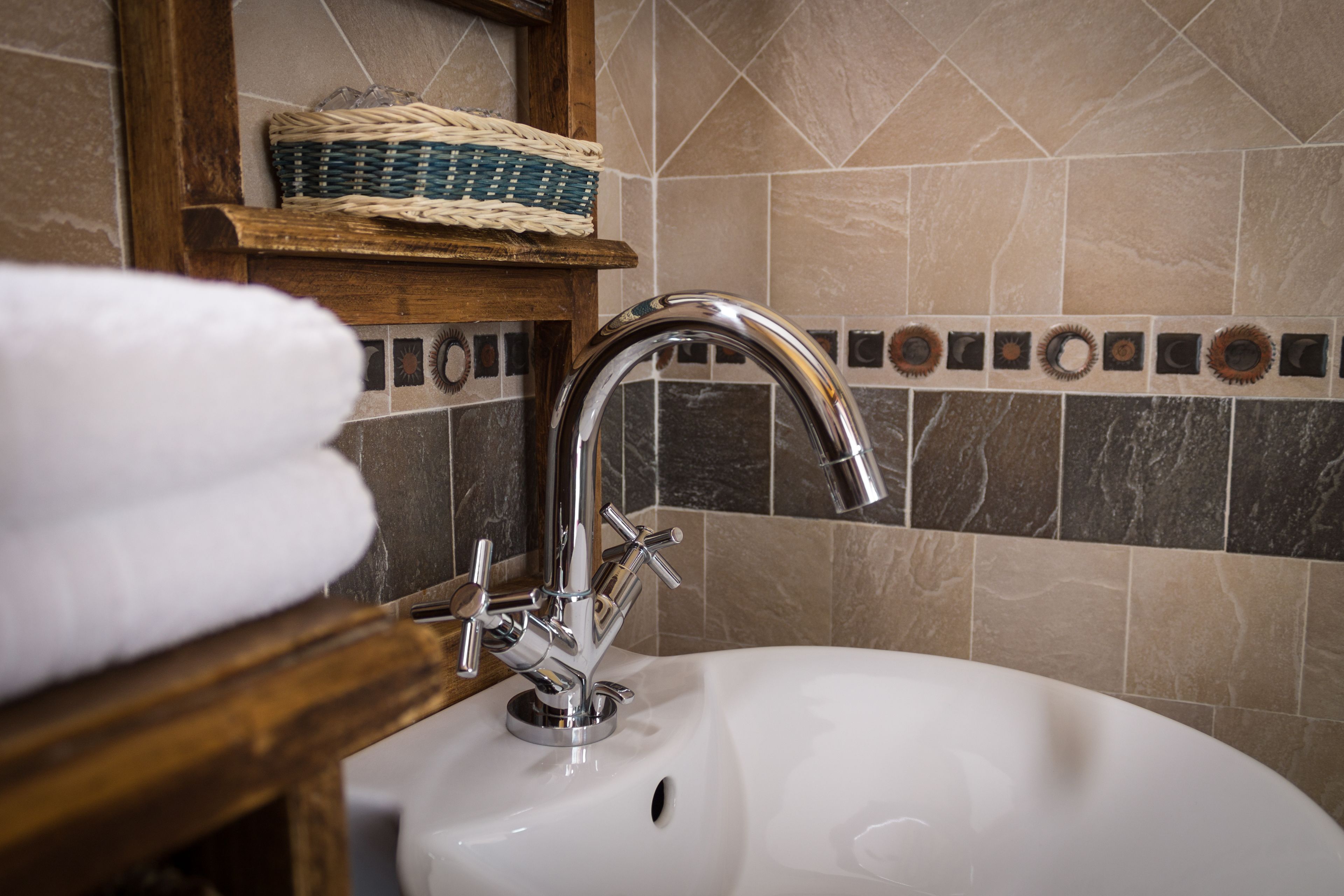A bathroom sink with a chrome faucet, a wooden shelf with a woven basket, and a tiled backsplash.