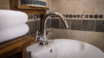 A bathroom sink with a chrome faucet, a wooden shelf with a woven basket, and a tiled backsplash.
