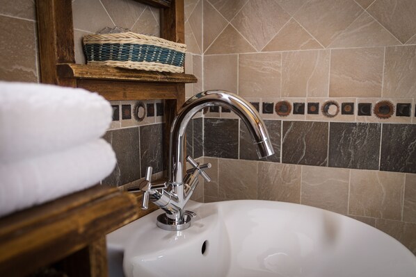 A bathroom sink with a chrome faucet, a wooden shelf with a woven basket, and a tiled backsplash. - La Carretería (Camanas)